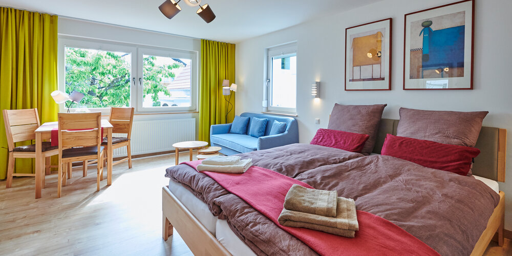 Ein Zimmer mit einem Bett und brauner Bettwäsche sowie mit einem blauen Sofa und einem kleinen Esstisch.