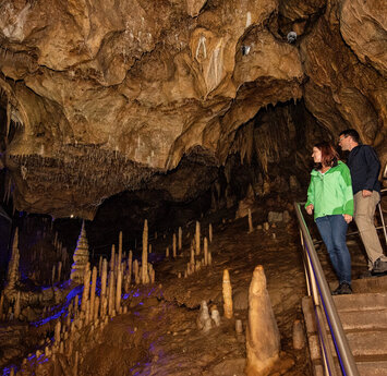 Ein Paar läuft lächelnd die Treppen in der Höhle hinab. Sie laufen an einer Vielzahl kleiner Tropfsteine vorbei.