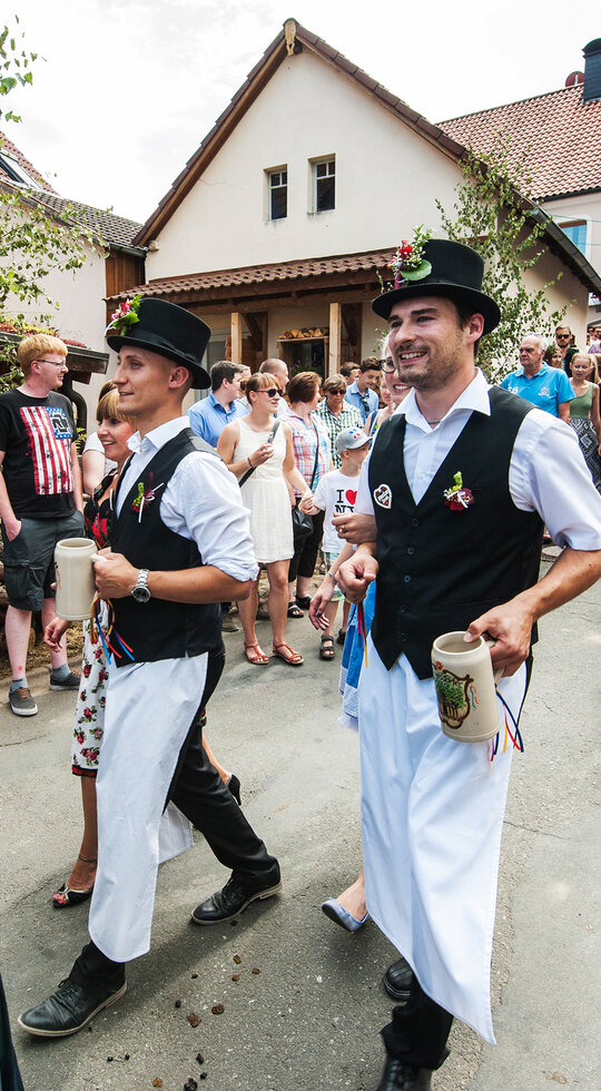 Viele lachende Menschen in fränkischer Tracht bei einem Festumzug. Die Männer tragen einen steinernen Bierkrug in der Hand.