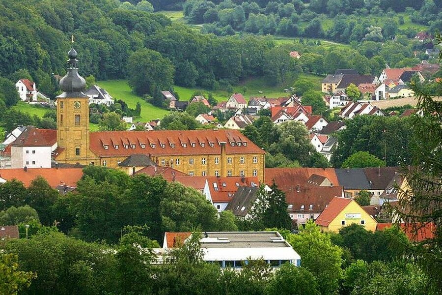 Von grünen Wäldern und Wiesen umgebener Ort mit einem großen Kloster in der Mitte.