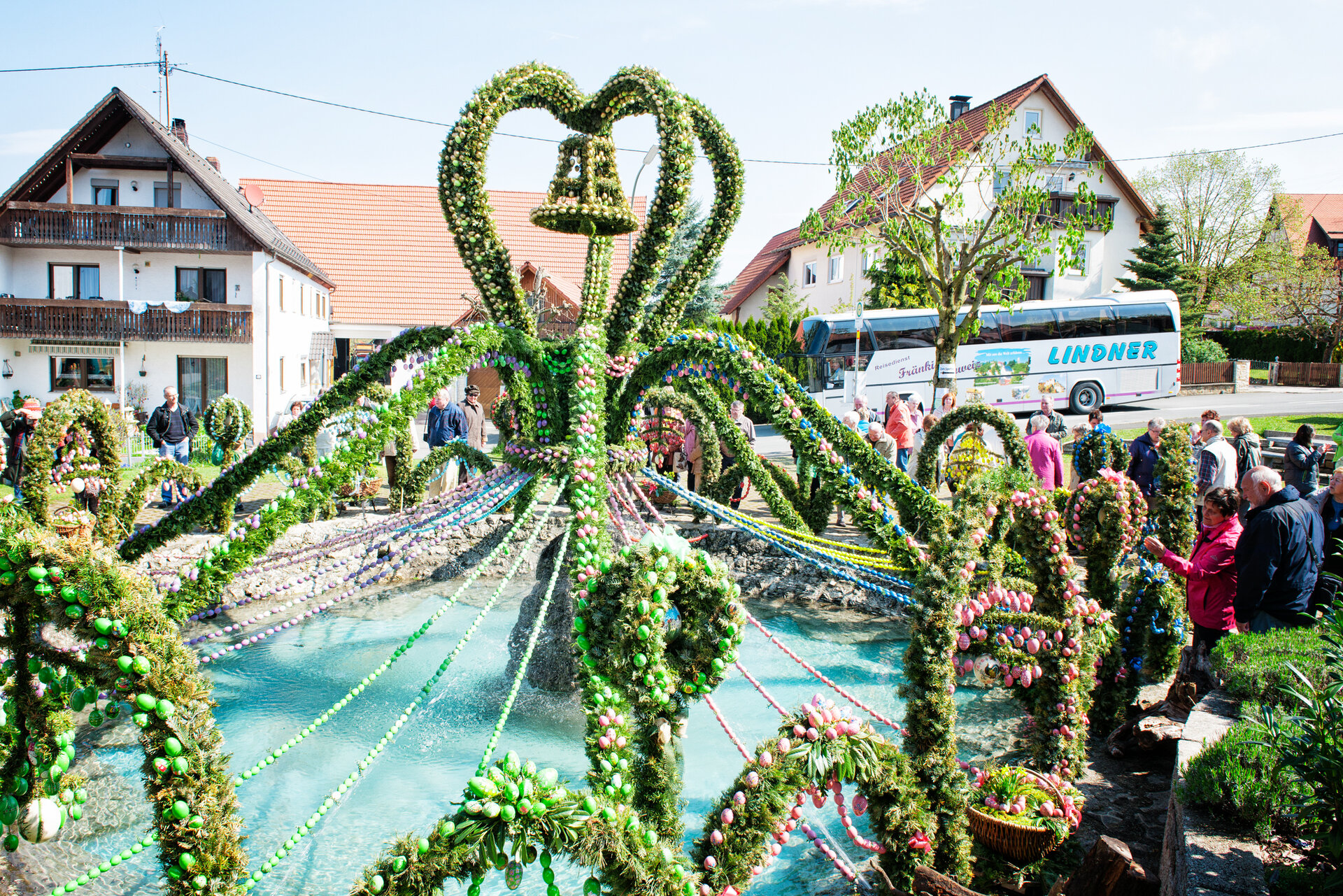 Ein bunt geschmückter Osterbrunnen mit vielen Ostereiern und grünen Girlanden wird von Besuchern bewundert.