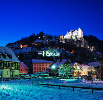 Blick auf den verschneiten Kurgarten bei Nacht. Im Hintergrund thront die beleuchtete Burg.