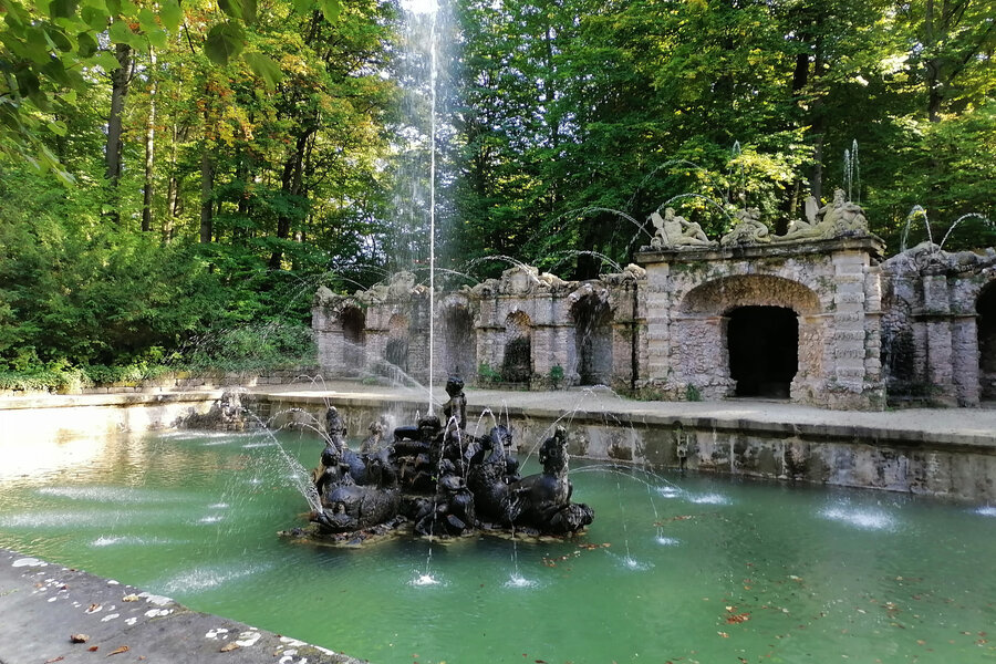 Eine Fontaine steigt aus einer Steinfigur in die Höhe.