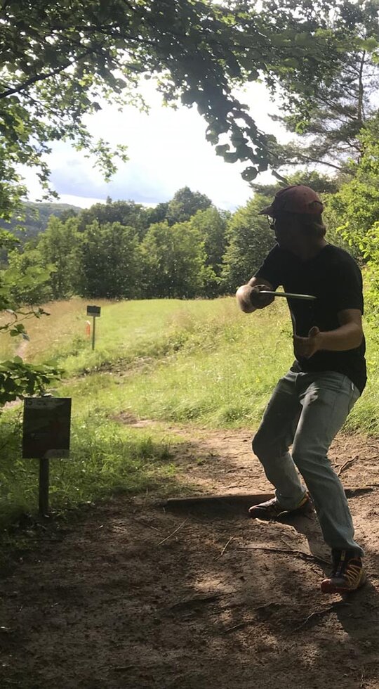 Ein Mann wirft eine Discgolfscheibe aus einem Wald hinaus.
