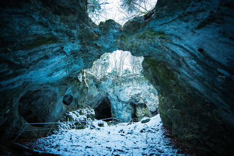 Ein Weg mit Metallgeländer führt durch eine oben teilweise offene Versturzhöhle. Oben im Bild berühren sich die Felsen und bilden eine Brücke.