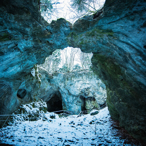 Ein Weg mit Metallgeländer führt durch eine oben teilweise offene Versturzhöhle. Oben im Bild berühren sich die Felsen und bilden eine Brücke.