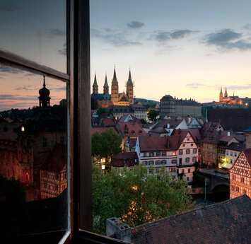 Blick durch ein offenes Fenster auf die Altstadt mit verwinkelten Gassen und dem Dom.