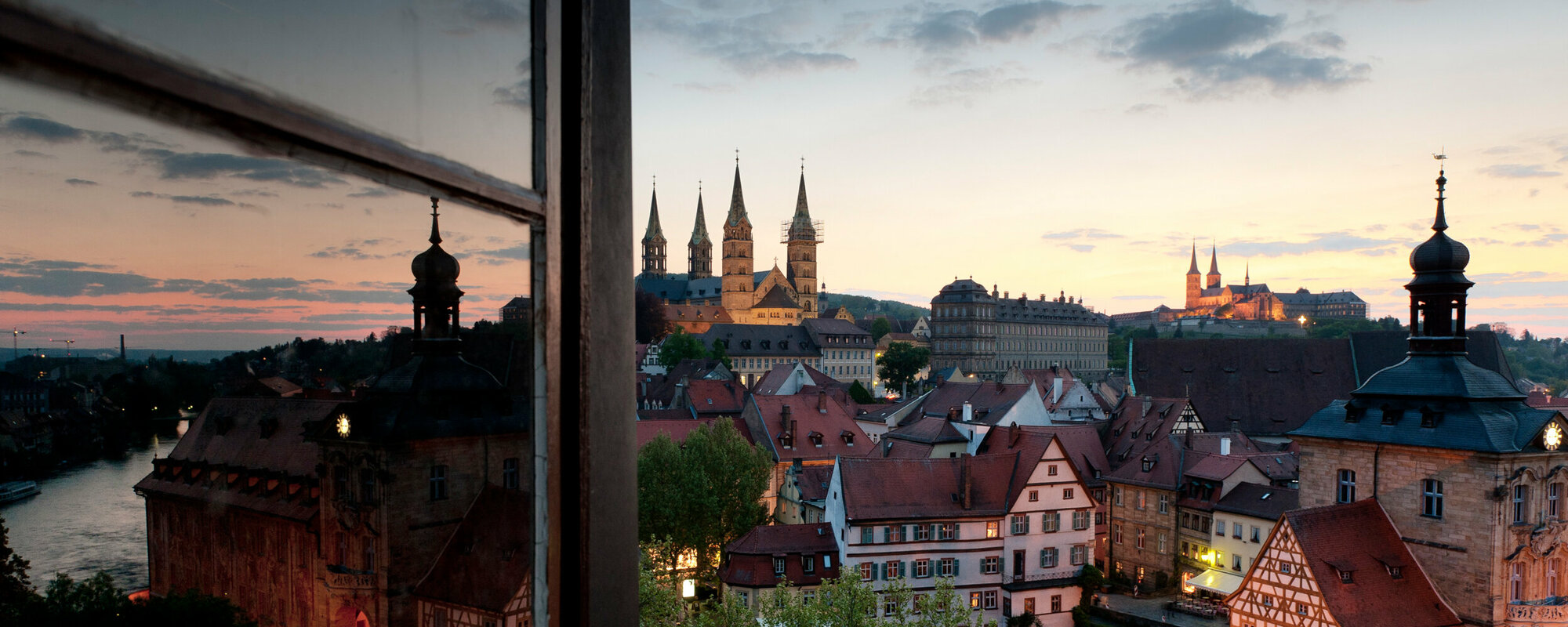 Blick durch ein offenes Fenster auf die Altstadt mit verwinkelten Gassen und dem Dom.