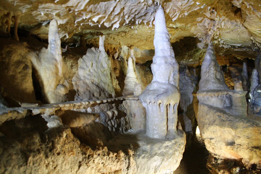In einer beleuchteten Höhle stehen mehrere Tropfsteine.
