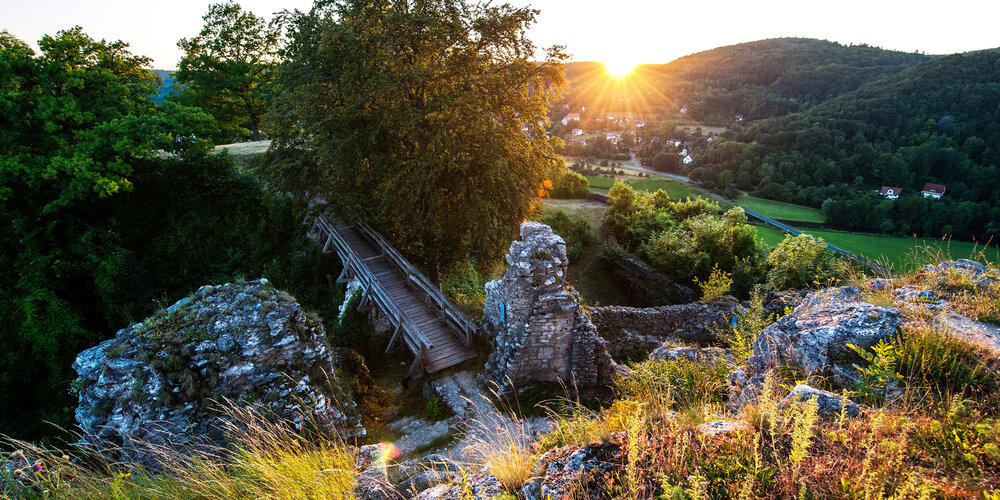 Eine hölzerne Brücke führt zu den Überresten der Burg. Im Tal stehen die Häuser von Streitberg.