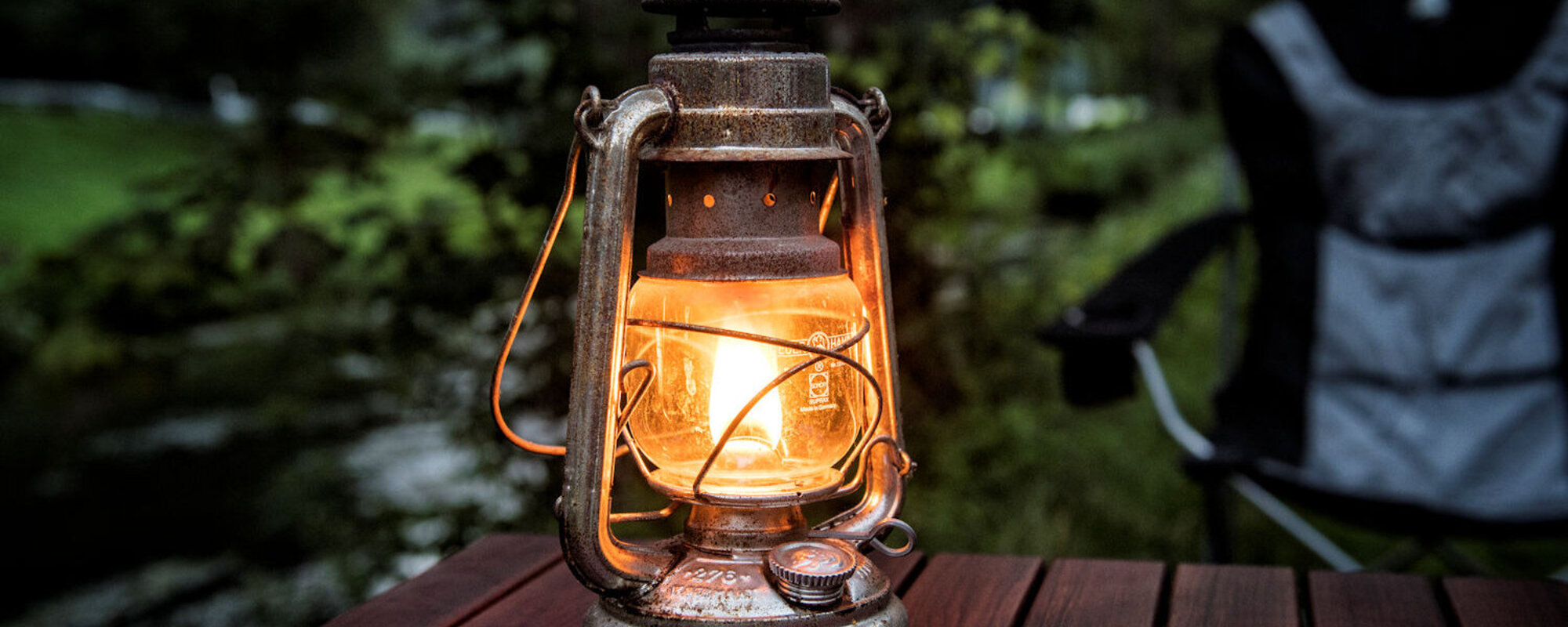 Eine brennende Öllampe steht auf einem hölzernen Campingtisch.