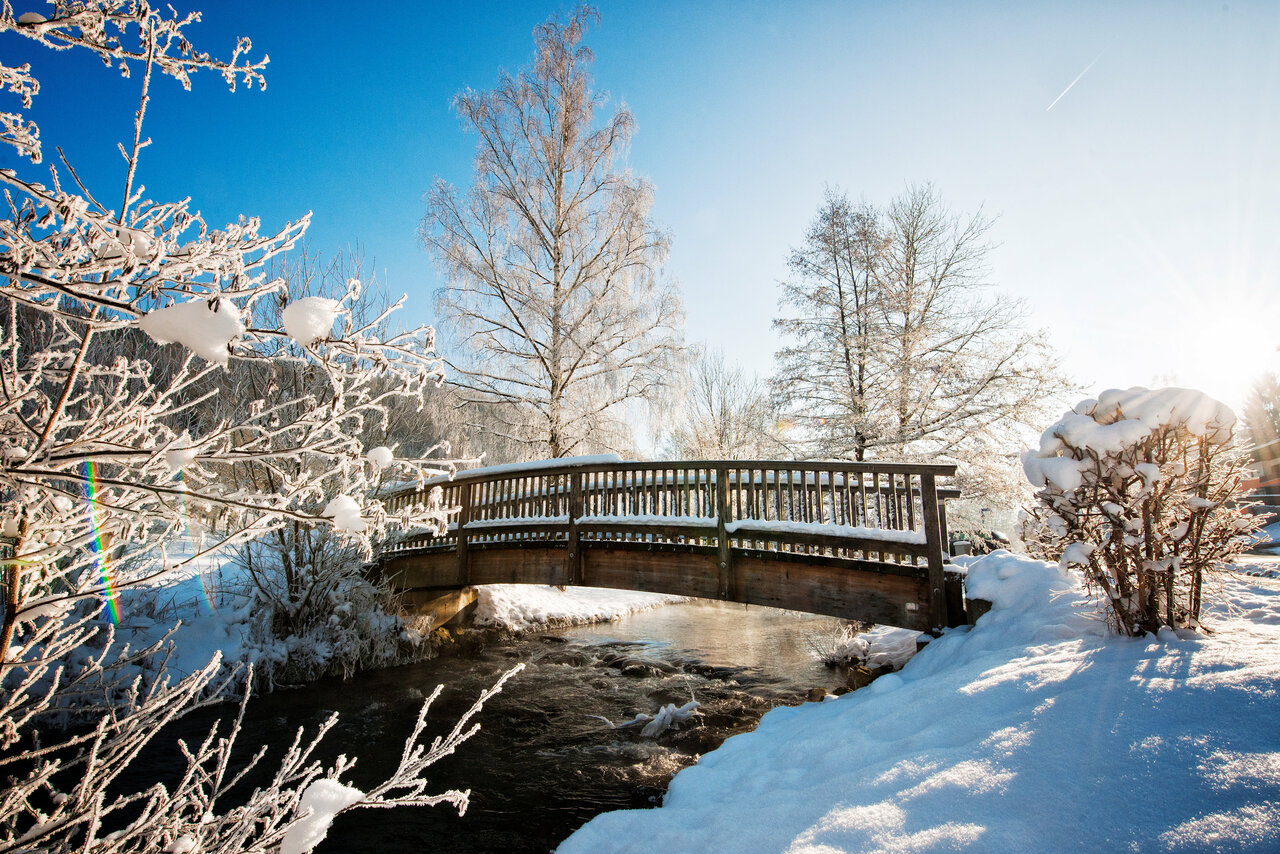 In idyllischer Winterlandschaft mit viel Schnee führt eine hölzerne Brücke über einen kleinen Fluss.