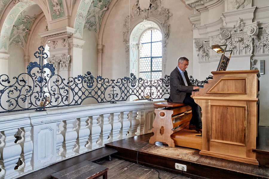 Ein Mann sitzt auf der Empore an einer Orgel in der Kirche und spielt darauf.