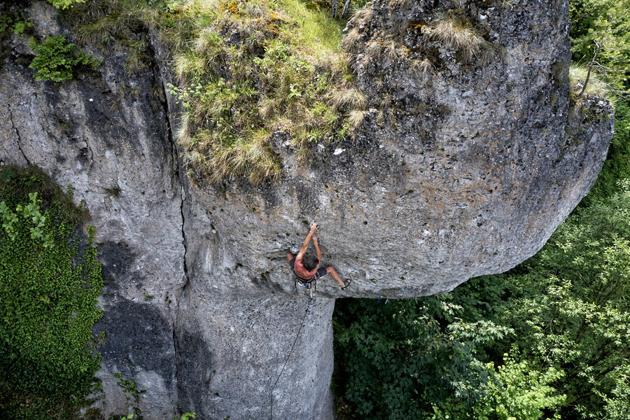 Ein Sportler mit freiem Oberkörber klettert an einem grauen Felsblock.