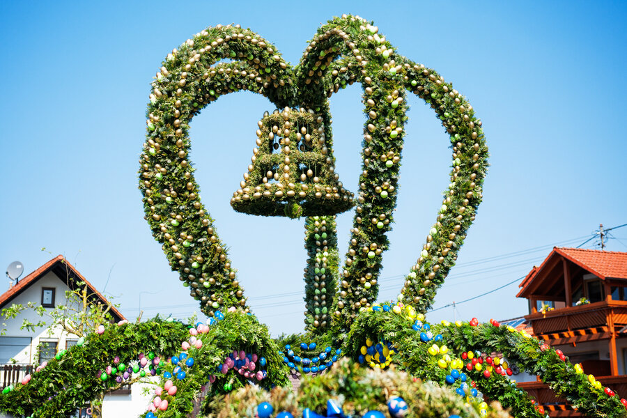 Eine aus grünen Zweigen gebastelte Krone auf dem Osterbrunnen. Sie ist mit goldenen Eiern geschmückt. In der Mitte der Krone hängt eine Glocke.