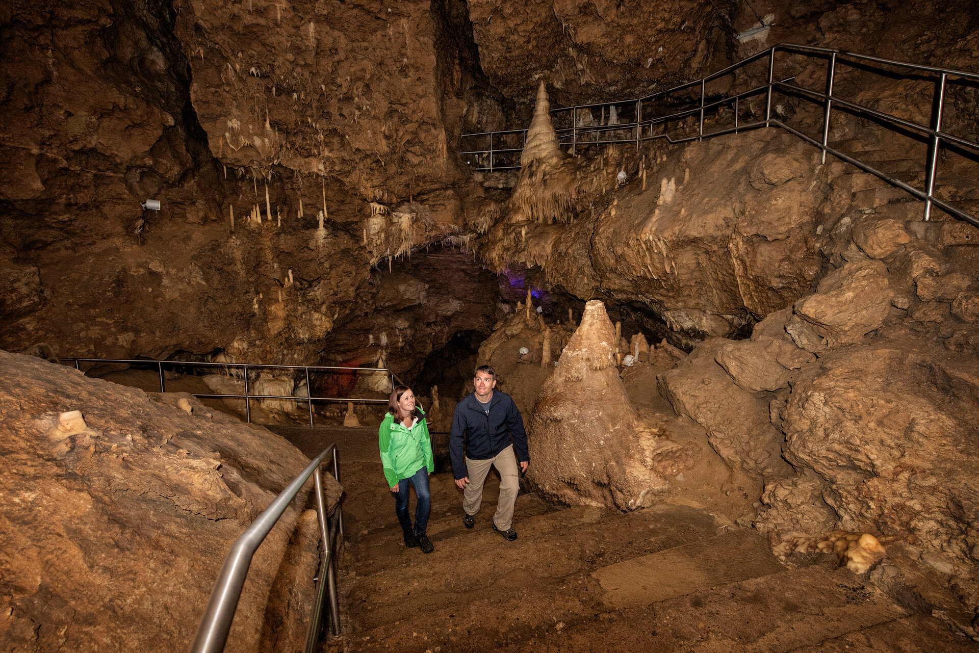 Ein Paar läuft lächelnd die Treppen in der Höhle hinauf. Sie befinden sich in einem großen Saal mit vielen Tropfsteinen und bewundern diese.