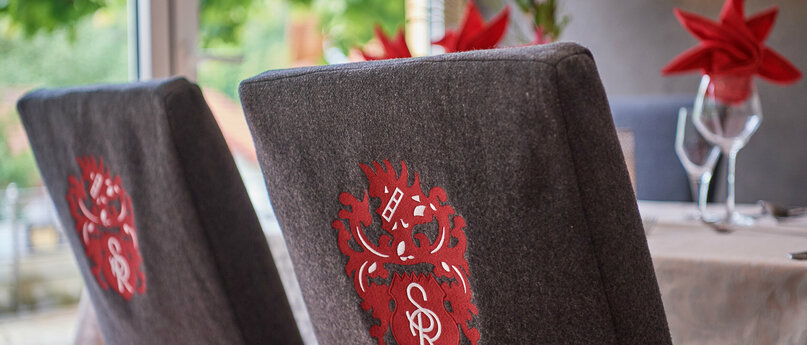 Rückansicht von zwei Stühlen mit grauen Hussen und roten Wappen.