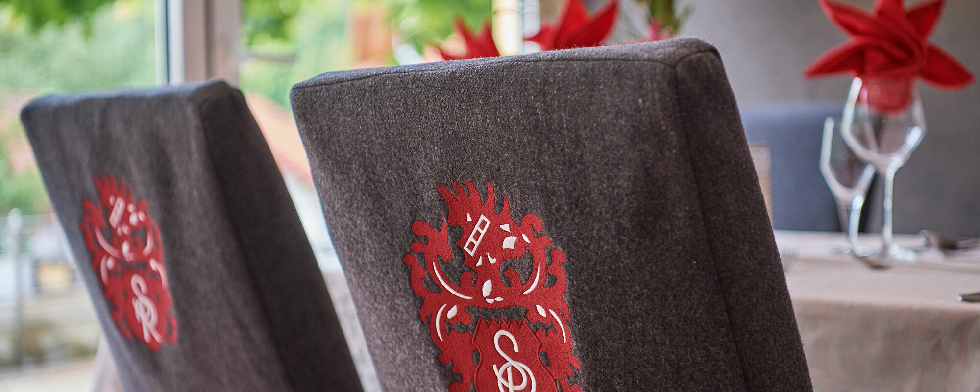 Rückansicht von zwei Stühlen mit grauen Hussen und roten Wappen.