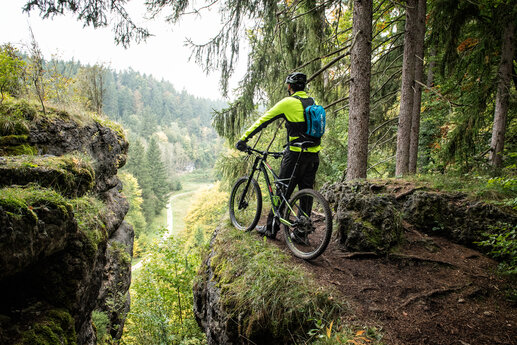 Ein Mann steht mit seinem Fahrrad am Abgrund eines Aussichtspunktes und blickt in das Tal hinab.