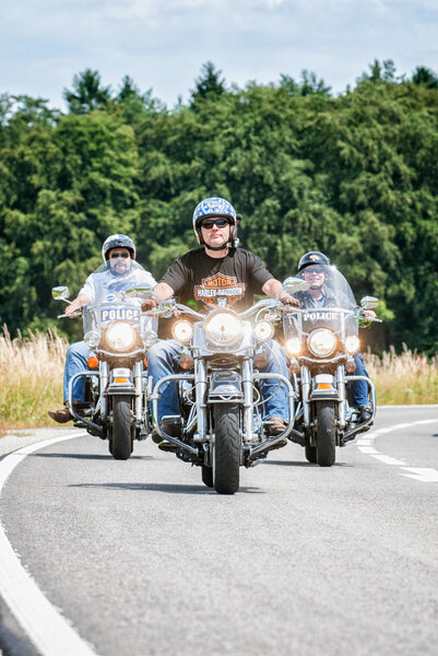 Drei Motorradfahrer fahren mit ihren Harleys auf einer Straße.