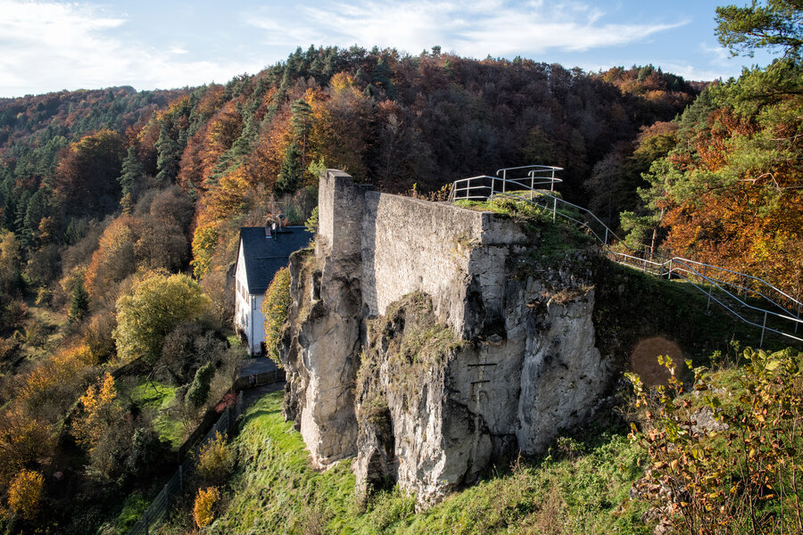 Im Herbstwald eingebettet liegt ein Aussichtspunkt in luftiger Höhe auf einem Felsen mit Stützmauer. Daneben steht ein Haus, dass wie an den Felsen geklebt wirkt.