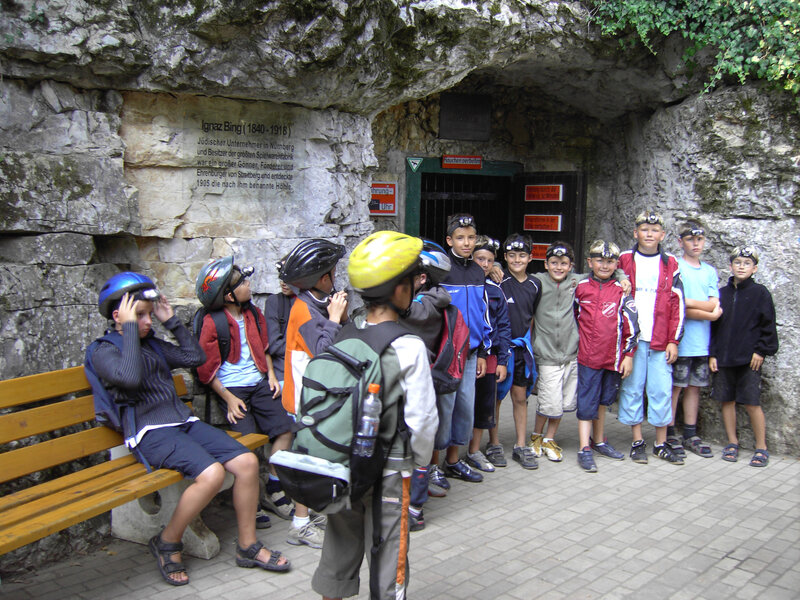 Eine Gruppe mit Kindern wartet im Freien vor dem Eingang einer Höhle.