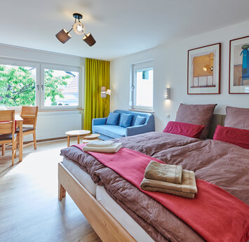 Ein Zimmer mit einem Bett und brauner Bettwäsche sowie mit einem blauen Sofa und einem kleinen Esstisch.