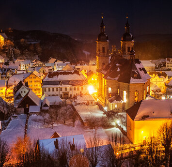 Nachtaufnahme der Burg und Kirche. Auf den Dächern des Ortes liegt Schnee. Die Beleuchtung der Straßen lässt das Bild weihnachtlich wirken.