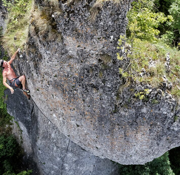 Vogelperspektive auf einen grauen Felsen, an dem ein Mann oben ohne klettert.
