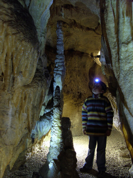 Ein Junge mit einer Stirnlampe steht in einer Höhle und leuchtet einen Tropfstein an.