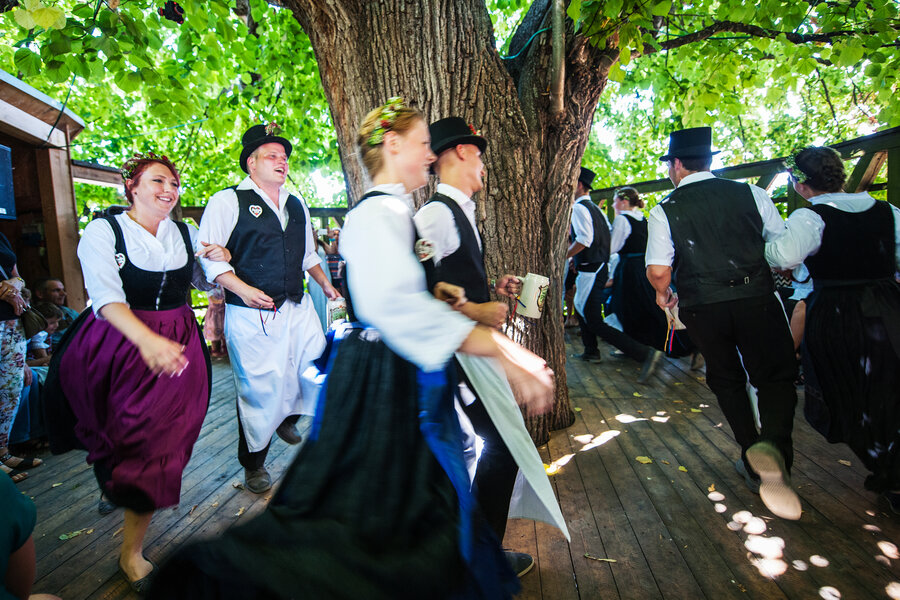 In fränkischer Tracht gekleidete Paare tanzen auf dem Tanzlindenboden um den Baum und lachen. 