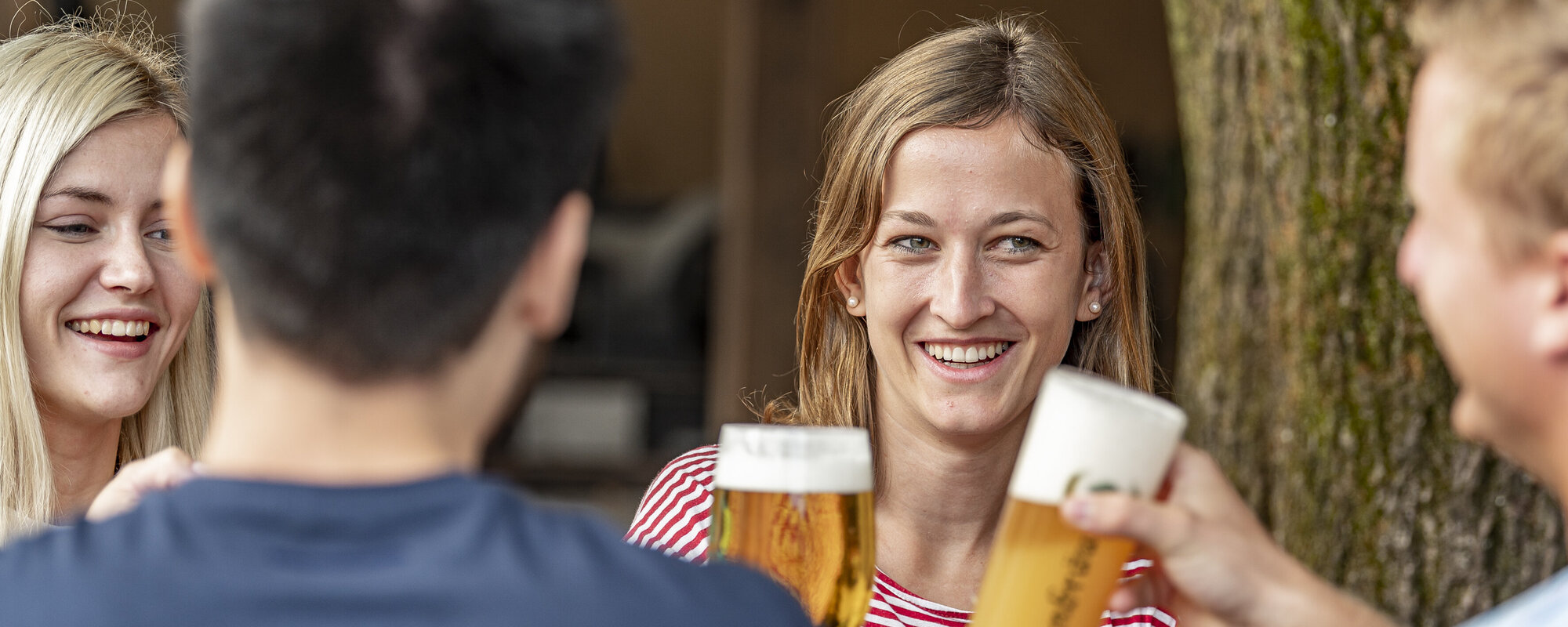Zwei lächelnde Frauen stoßen mit zwei Männern mit einem Bier an.