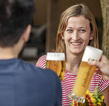Zwei lächelnde Frauen stoßen mit zwei Männern mit einem Bier an.