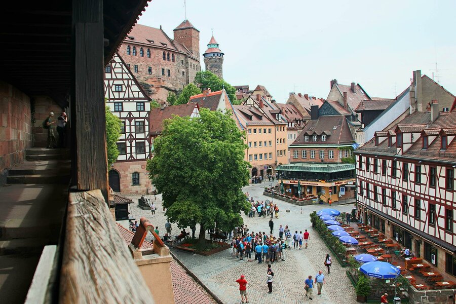 Ein blebter, gepflasterter Platz in der Altstadt. Im Hintergrund ist ein Turm der Burg.