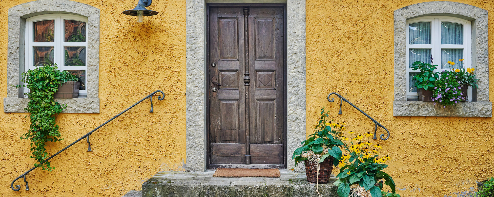 Eine alte hölzerne Eingangstür führt über Steintreppen in ein gelbes Haus.