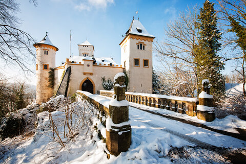 Eine steinerne Brück führt hinüber zum Eingangstor des Schlosses. Der Schnee leuchtet hell und die Sonne scheint.