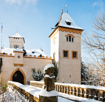 Eine steinerne Brück führt hinüber zum Eingangstor des Schlosses. Der Schnee leuchtet hell und die Sonne scheint.