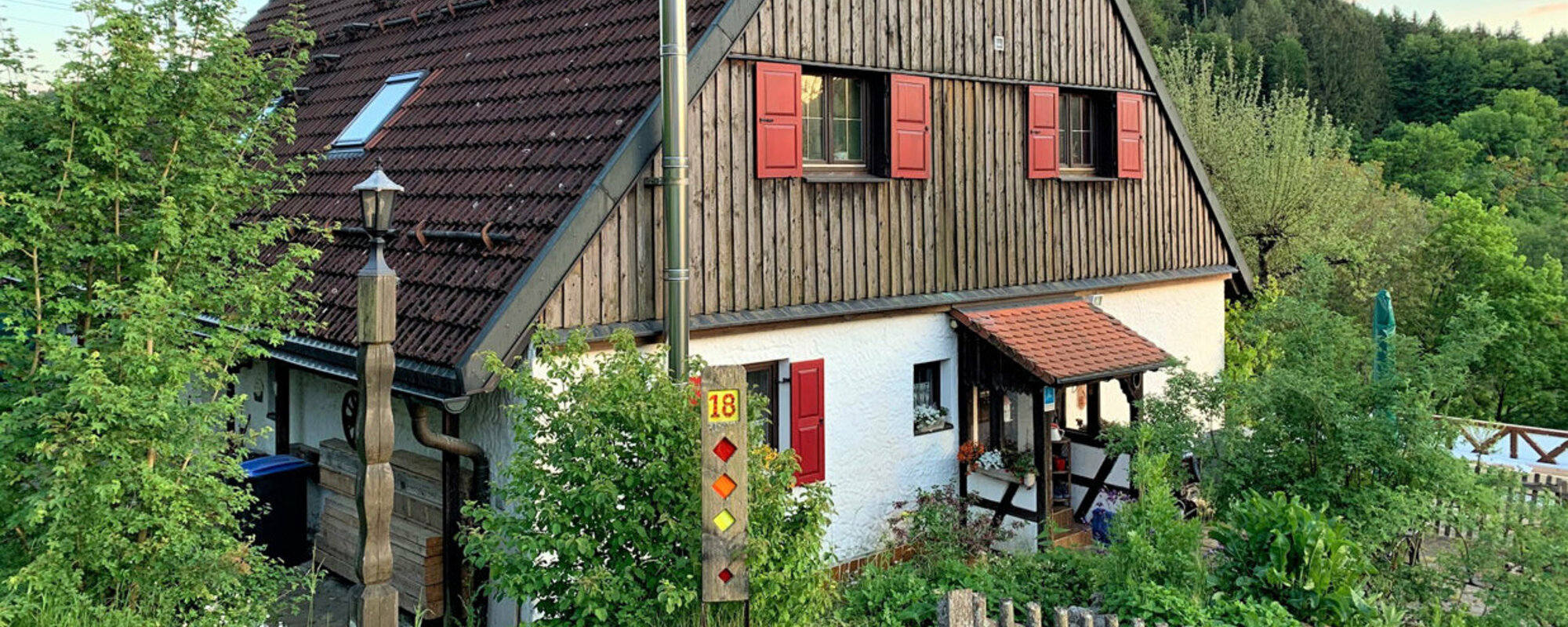 Ein Haus im Grünen mit hölzerner Fassade im oberen Bereich und roten Fensterläden.